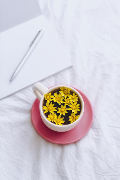 Yellow¡up mit gelben Blumen im Inneren, auf einem weißen Bett mit Notizblock und Stift.