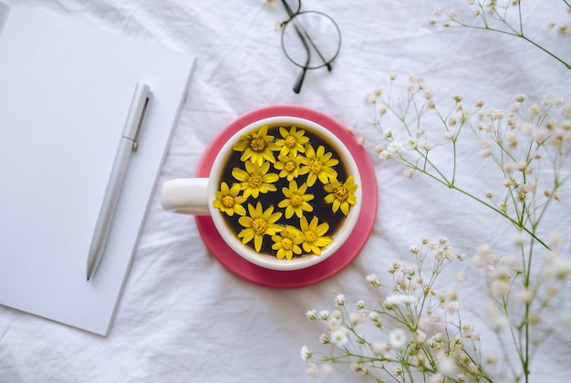 Yellow¡up mit gelben Blumen im Inneren, auf einem weißen Bett mit Notizblock und Stift.