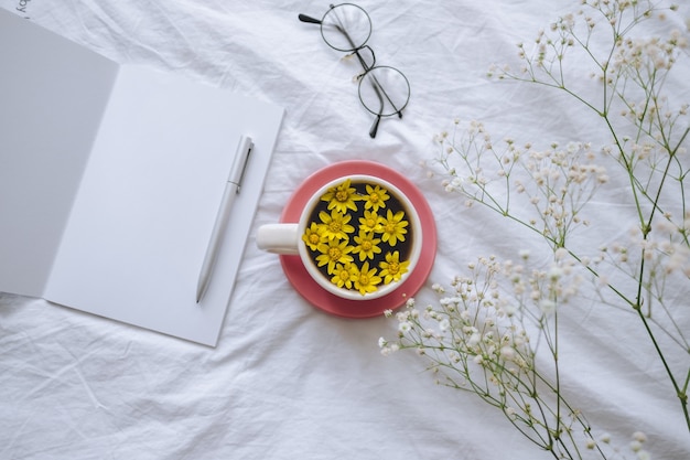 Yellow¡up mit gelben Blumen im Inneren, auf einem weißen Bett mit Notizblock und Stift.