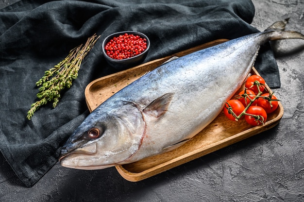 Foto yellowtail japonês cru inteiro fresco com tomate e ervas. fish amberjack. fundo preto. vista do topo.