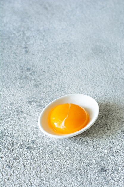 Yema de huevo en un tazón blanco sobre un fondo gris. Huevo. Producto para cocinar.