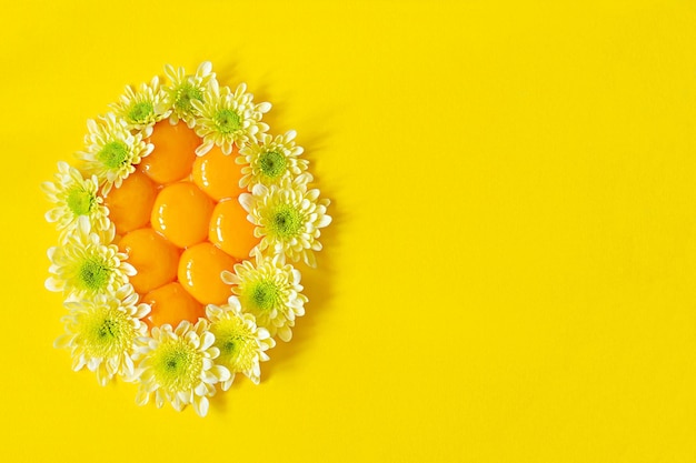 Yemas crudas frescas dispuestas en forma de huevo decoradas con flores sobre un fondo amarillo Concepto inusual de Pascua Alimentos que contienen proteínas