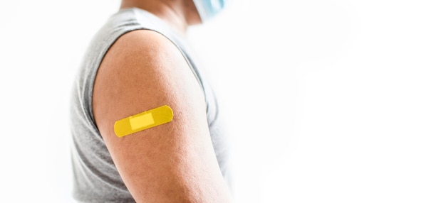 El yeso amarillo está unido al brazo del hombre Concepto de primeros auxilios después de la vacunación contra el coronavirus COVID-19 y la aguja médica profesional cáncer de sangre Closeup fondo borroso blanco