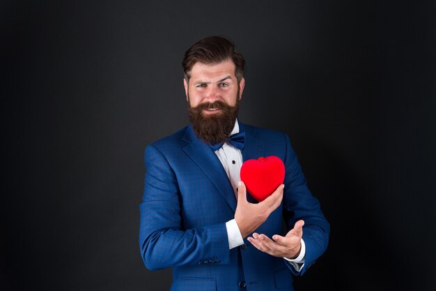 Yo creo en el amor. Feliz día de San Valentín. esmoquin hombre corazón rojo. cita de amor. barba hipster madura en traje formal. problemas con el corazón. empresario con pajarita. problemas con el corazón. Saludo romántico.