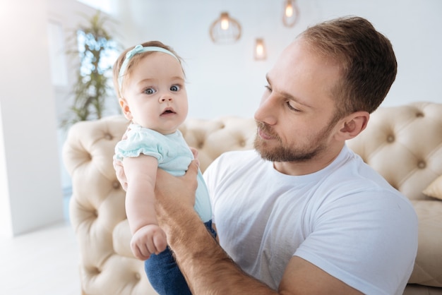 Yo y mi padre. Divertida hija agradable encantadora de pie cerca de su joven padre y mirando a otro lado mientras expresa interés y positividad