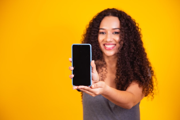 Yo recomiendo. Chica afroamericana sorprendida apuntando a la pantalla del teléfono en blanco. Copiar el espacio