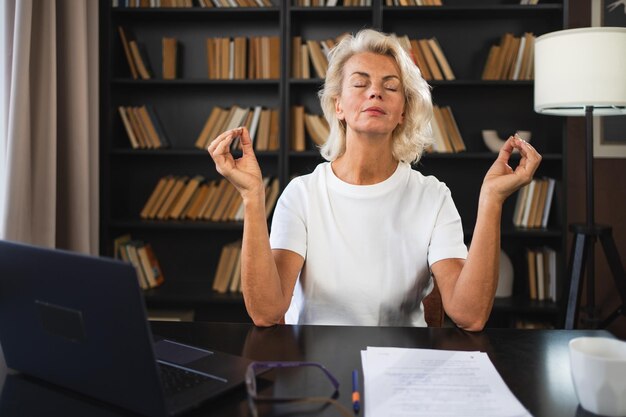 Yoga, Achtsamkeit, Meditation, kein Stress, ruhig bleiben, mittelalterliche Frau übt Yoga im Büro, Frau