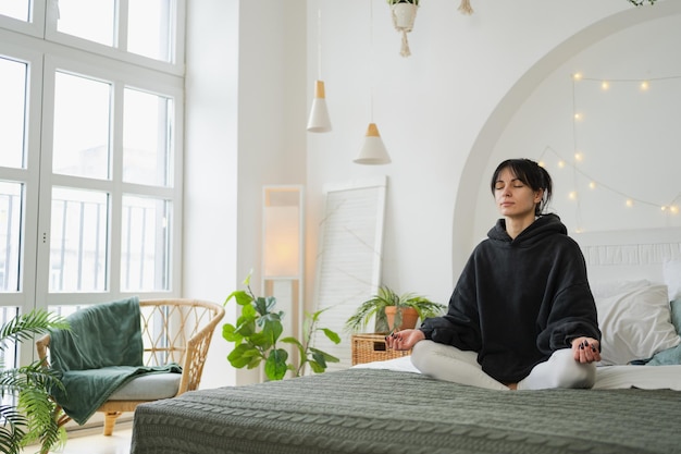 Foto yoga-achtsamkeitsmeditation junge gesunde frau übt yoga im schlafzimmer zu hause frau sitzt in