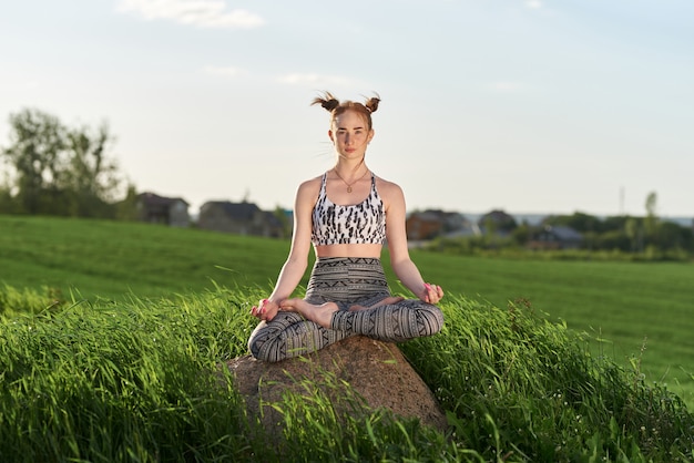 Yoga al aire libre. Mujer feliz haciendo ejercicios de yoga, meditar en el parque soleado. Concepto de estilo de vida saludable y relajación. Linda mujer practicando yoga en pasto