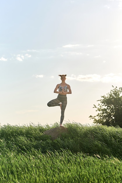 Yoga al aire libre. Mujer feliz haciendo ejercicios de yoga, meditar en el parque soleado. Concepto de estilo de vida saludable y relajación. Linda mujer practicando yoga en pasto