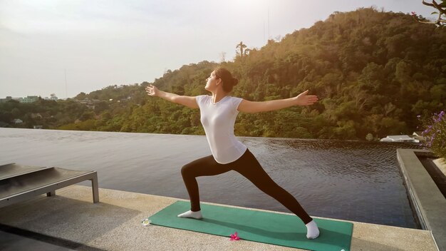 Yoga al aire libre. Mujer en una pose de guerrero cerca de la luz del sol de la piscina