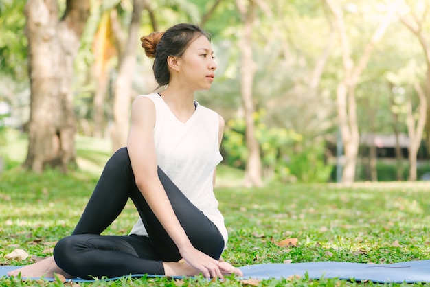 La yoga asiática joven de la mujer al aire libre guarda calma y medita mientras que practica yoga