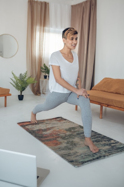 Yoga en casa. Chica joven de pelo corto haciendo yoga en casa y mirando concentrado