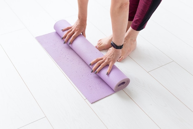 Yoga, concepto peopel - Cerca de mujer rodando su estera después de una clase de yoga