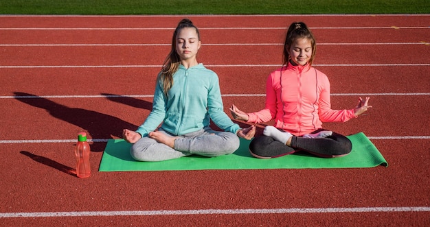 El yoga da energía a las adolescentes que practican yoga en la estera, la meditación al aire libre está en armonía con el estado físico del cuerpo calentándose en el gimnasio del estadio, los niños de pilates entrenan en la lección de educación física de la escuela