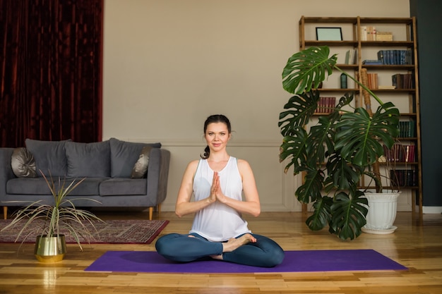 Yoga-Frau sitzt in einer Lotussitzposition auf einem Teppich in einem Raum