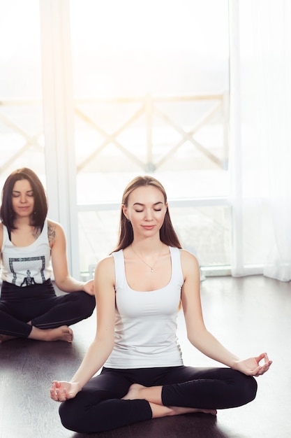 Yoga-Gruppenkonzept Junges Paar meditiert zusammen sitzend Rücken an Rücken in der Nähe von Fenstern