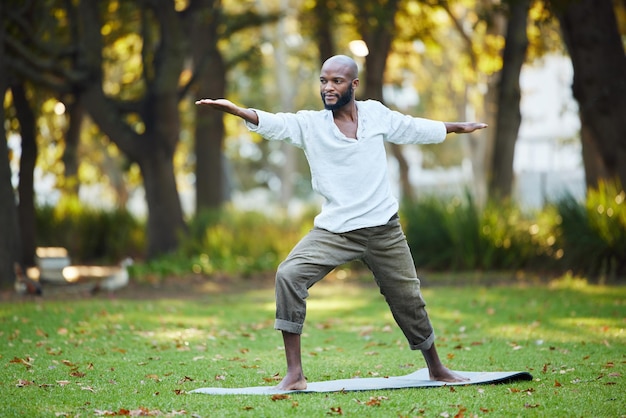 Yoga hält ihn in Form Ganzkörperaufnahme eines hübschen jungen Mannes, der draußen im Park Yoga praktiziert