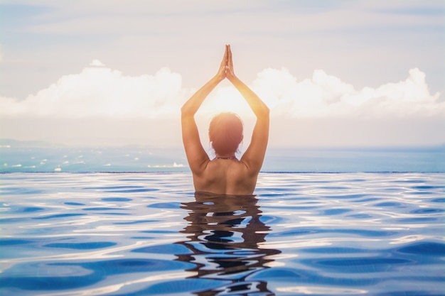 Yoga hermosa mujer en piscina azul turquesa.