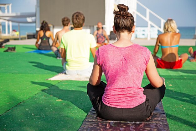 Yoga im Park, junge Frau macht Übungen mit einer Gruppe von Menschen unterschiedlichen Alters.