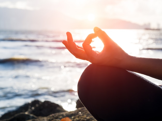 Yoga-Konzept Übende Lotoshaltung der Nahaufnahmefrauenhand auf dem Strand bei Sonnenuntergang.