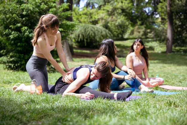 Yoga-Kurs im Park. Ein Lehrer hilft einem der Mädchen, während der Rest sich ausruht. Konzept von Gesundheit und Wellness.