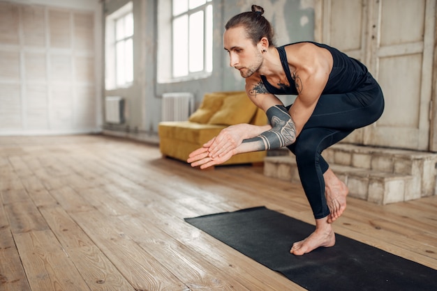 Yoga masculino haciendo ejercicio de equilibrio en la colchoneta en el gimnasio