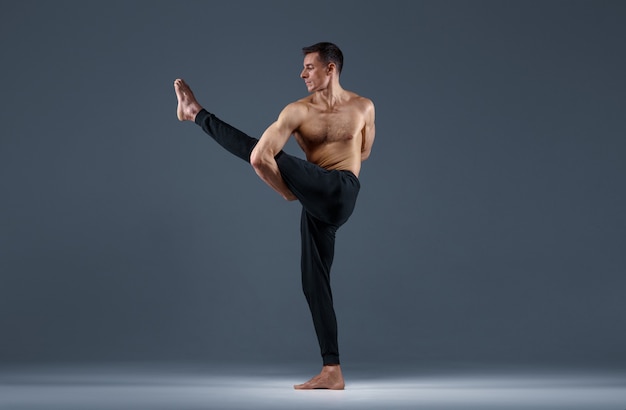 Yoga masculino haciendo ejercicios de estiramiento sobre fondo gris. Hombre fuerte practicando yogui, entrenamiento de asanas, máxima concentración, estilo de vida saludable