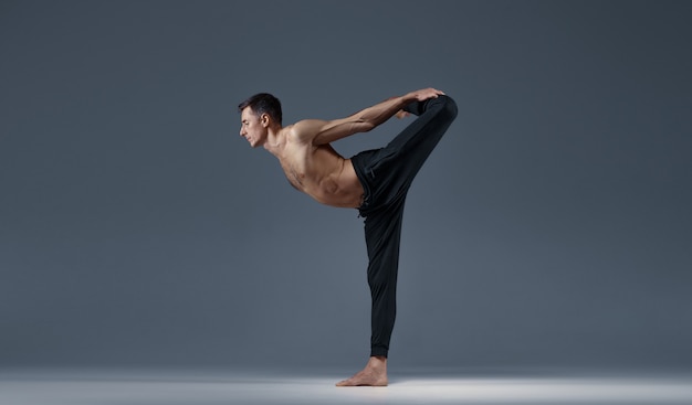 El yoga masculino mantiene el equilibrio en una pose difícil, pared gris Hombre fuerte haciendo ejercicio yogui, entrenamiento de asanas, concentración superior, estilo de vida saludable