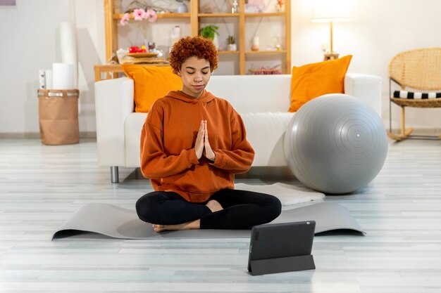 Yoga mindfulness meditación joven niña africana sana practicando yoga en casa mujer sentada en lotu