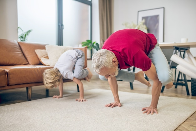 Yoga mit Sohn. Grauhaariger, fitter Mann, der zusammen mit seinem Sohn Yoga macht