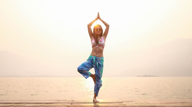 Yoga en la playa Mujer asiática feliz con bikini Tie Dye practicando yoga Mujer sana joven en yoga de verano al atardecer