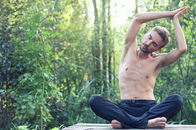 Yoga practicante del hombre barbudo joven al aire libre. Bosque verde en el fondo