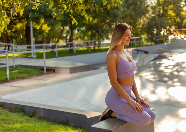 Yoga praktizieren. Meditation bei Sonnenaufgang. Junge schlanke Frau, die im Lotussitz draußen sitzt. Gesundes Lebensstilkonzept