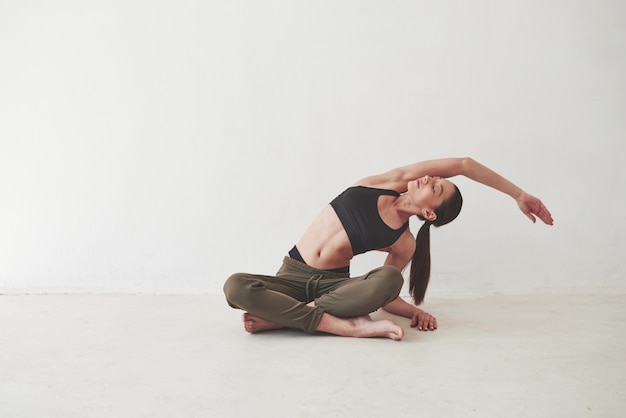 Foto yoga-übungen machen. kaukasische hübsche frau steht gegen leerraum im leeren raum