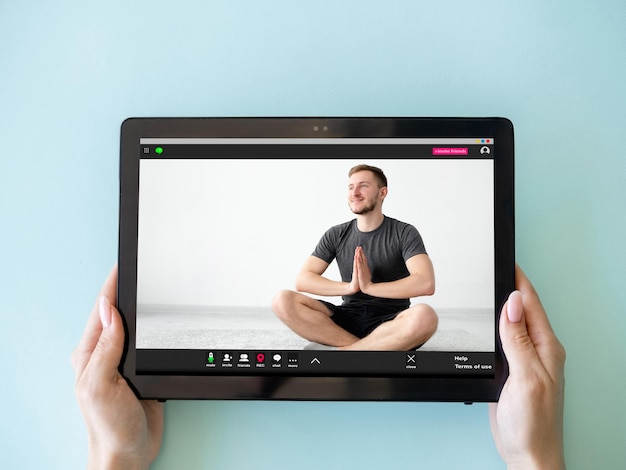 Foto yoga-videokurs online-meditation virtuelles training frauenhände, die ein tablet mit einem entspannten mann in lotus-pose auf dem bildschirm halten, isoliert auf blau