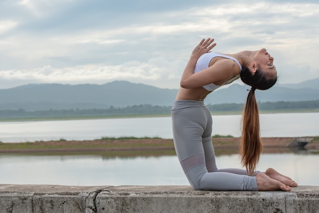 Yogafrau, die Yogahaltung auf der Wand mit Reservoirhintergrund tut.