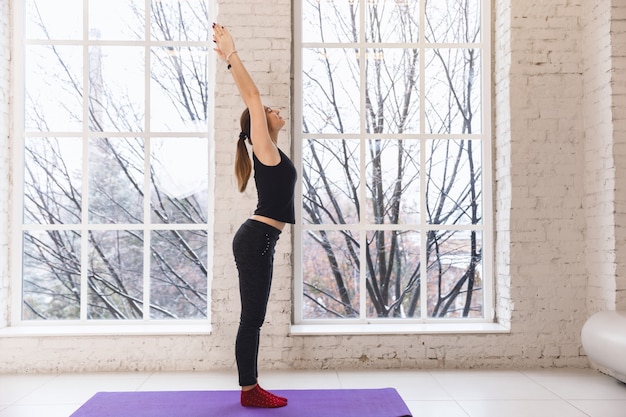 Yogamädchen allein im Yogaraum am Fenster morgens stehend mit den Händen oben