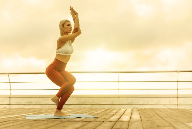 Yogapraxis bei Sonnenaufgang. Junge Yogifrau steht morgens in Baumpose am Strand