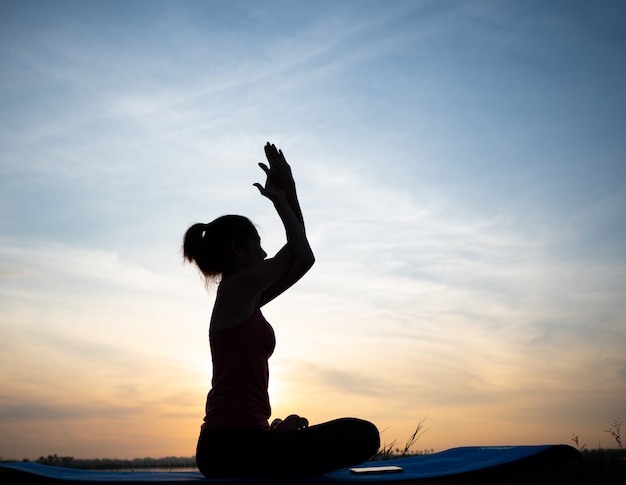 Yogastellungsposition mit Morgenlicht und weichem blauem Himmel, eine schlanke Trainerdame mit ihrer durchführenden Art der Yogabehandlung.