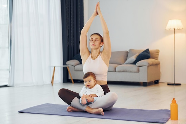 Yogaübungen machen Mutter mit ihrer kleinen Tochter ist zusammen zu Hause