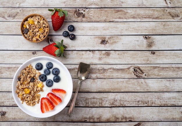 Yoghurt con fresa, arándano y granola en un tazón sobre una mesa de madera con espacio para copiar