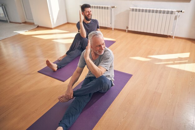 Yogis caucásicos profesionales alegres que realizan el medio señor de los peces posan en la estera