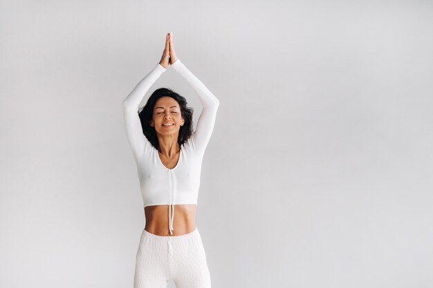 Una yogui vestida de blanco con las manos en alto medita en la sala de yoga