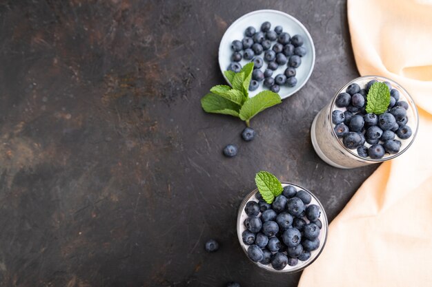 Yogur con arándanos y chía en vidrio sobre superficie de hormigón negro y textil de lino naranja