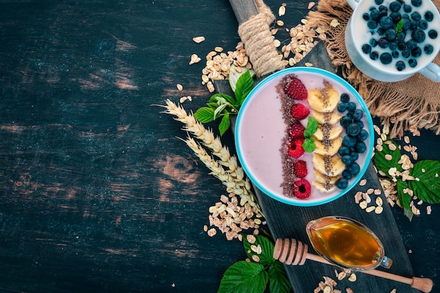 Yogur con arándanos, frambuesas y plátano En el plato Sobre un fondo de madera Vista superior Espacio libre para texto