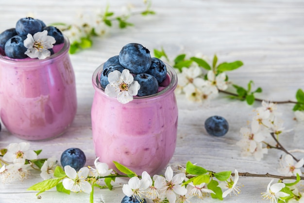 Yogur de arándanos o yogur en vasos servidos con arándanos frescos y flores de cerezo en flor de primavera