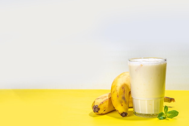 Yogur de batido de plátano o cóctel de batido bebida orgánica saludable con plátanos frescos en el espacio de copia de fondo amarillo brillante