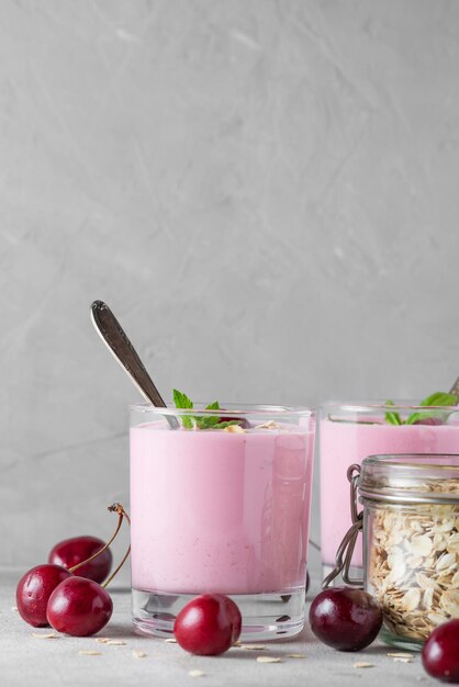 Yogur de bayas de cereza en vasos con bayas frescas avena menta para un desayuno saludable sobre fondo gris Orientación vertical