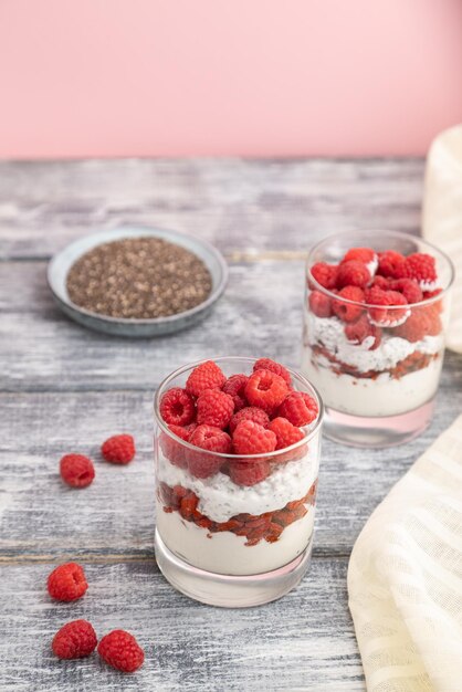 Yogur con bayas de goji de frambuesa y semillas de chía en vidrio sobre fondo de madera gris Vista lateral enfoque selectivo